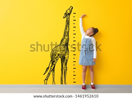 Surprised African-American girl measuring height near color wall with drawn giraffe
