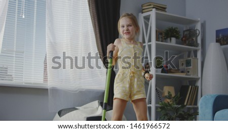 Medium shot of girl singing and using broom handle as microphone