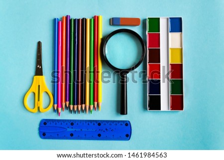 A set of school supplies. Magnifying glass, pencils, ruler, sheath, watercolor on a blue paper background with space for text. Flat lay