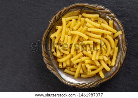 Lot of whole raw pasta macaroni in old iron bowl flatlay on grey stone