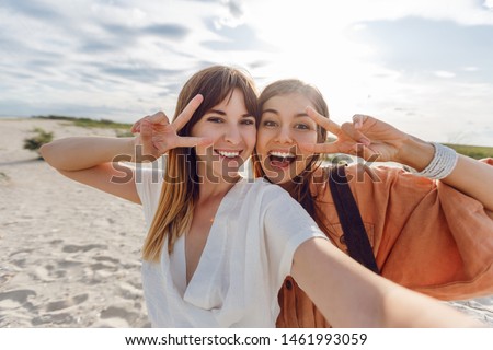 Two blissful cute girls  making self portrait on amazing tropical beach.   Friends shows signs and enjoying  vacation. Summer time. 