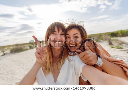 Two  crazy  girls  making self portrait on amazing tropical beach.   Friends shows signs and enjoying  vacation. Summer time. 