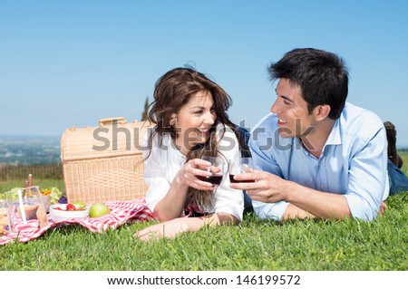 Portrait Of Happy Young Couple Lying On Grass And Enjoying Wine