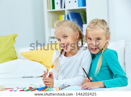 Portrait of lovely twins with colorful pencils looking at camera