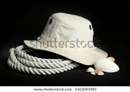 Cotton wide brim men's canvas safari travel hat and a heavy climbing rope with an assortment of sea shells on a black background
