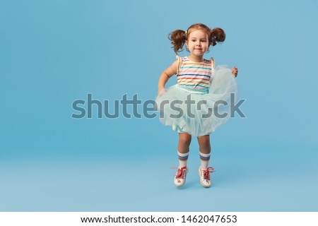 Little happy toddler child girl dreams of becoming ballerina in a cyan tutu skirt. Blue background. Space for text Royalty-Free Stock Photo #1462047653
