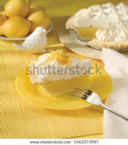 Slice of lemon meringue pie with whole pie and whole lemons in background 