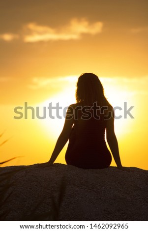 silhouette of beautiful thoughtful girl sitting on the sand and enjoying the sunset, the figure of young woman on the beach, female meditate on nature
