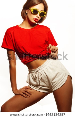 Women's summer clothing concept. Portrait of young beautiful girl wearing red t-shirt, trendy eyewear, white shorts isolated on white background. Beach style. Studio shot