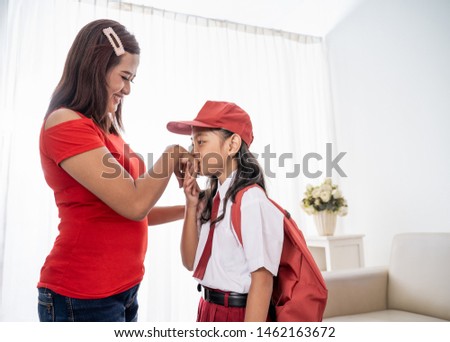 kid kissing mother's hand while shaking hand before going to school. indonesian school uniform