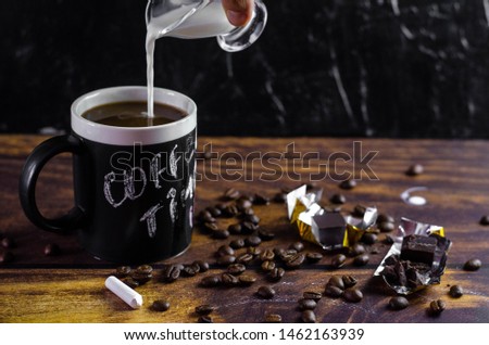 coffee in a big black cup with coffee time title. dark background with coffee beans and chocolate. milk in a small glass pot
