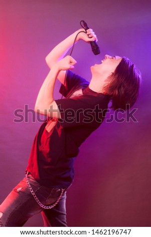 The young guy is singing and screaming in microphone on stage, concert concept.