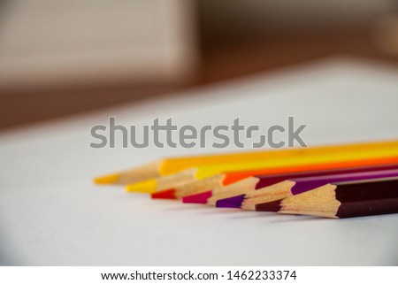 six multi-colored pencils lie in a row on white sheets of paper