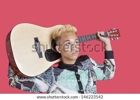 Teenage boy carrying guitar over his shoulder over pink background