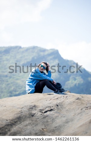 woman wearing blue sunglasses sitting on rock with lovely smile, mountain background
