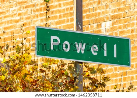 Powell street sign on pole in San Francisco, California. Green meatl plate, white writing/ lettering. Brick wall building in background.