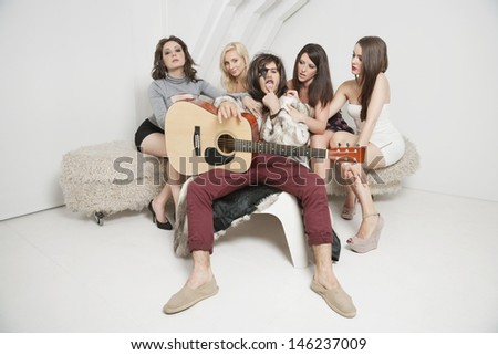 Portrait of young male guitarist sitting amid young female friends