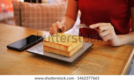 Business woman eating a piece of bread Toast by knife and fork. Garlic Bread, hot coffee and smartphone on wooden table. Popular breakfast of the common people Provide enough calories to the body. 