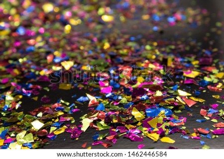 This is a photograph of a metallic colorful confetti placed on a Black background