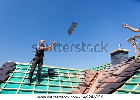 Two roofers transfer tiles across the roof by tossing them through the air