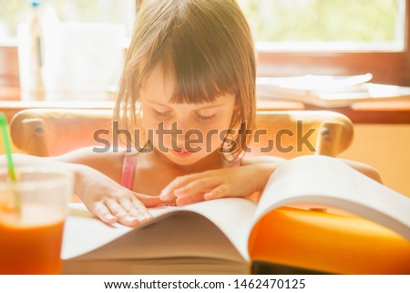 Cute little child girl flipping with interest a book about world history of photography. Horizontal image.