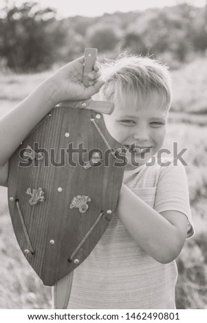 Black and white vertical image of cute happy kid playing outside with toys. Boy standing in beautiful sunny sunset landscape.