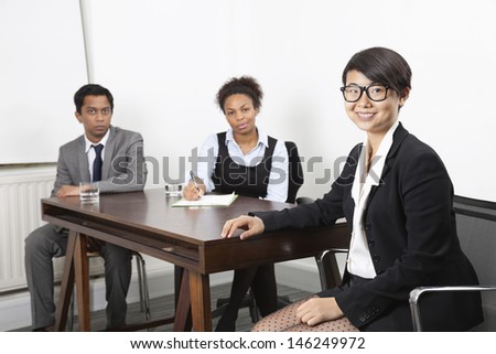 Portrait of Asian female with multiethnic colleagues in background at desk in office