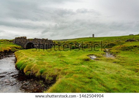 Irish countryside landscape with a old stone bridge and the castle Doonagore in the background on the coastal walk route from Doolin to the Cliffs of Moher, Wild Atlantic Way, county Clare in Ireland