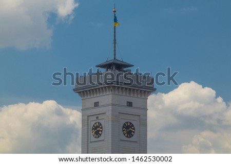 Detail of city hall tower in Lviv, Ukraine, centered in the middle of the picture on a sunny day with blue skies and some clouds. People seen on top