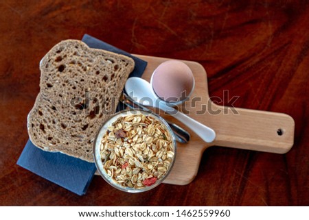 Healthy and simple breakfast, A bowl of yoghurt with muesli and cereal dish based on rolled oats and ingredients like grains, nuts, seeds and fresh or dried fruits on top, Brown bread and boiled egg.