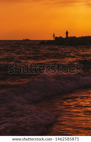 Fishing during sunset time in sea water. Vertical color photography.