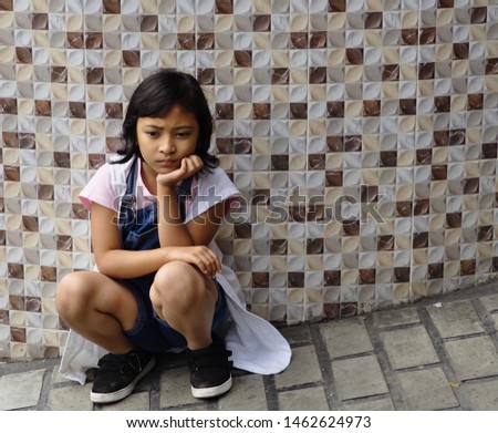 A little girl leaning back to the wall sitting with sullen face.