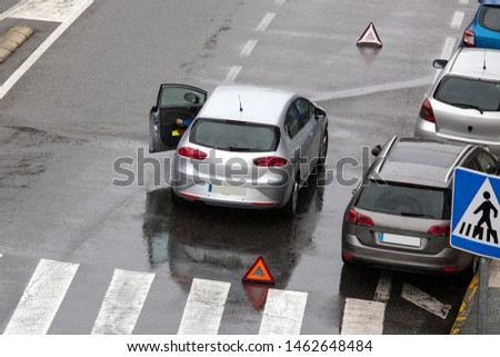 Scene of a broken down car on a city street road near a crosswalk with and a red triangle to warn other road users. Rainy day. Copy space