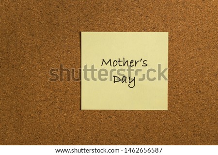 Small yellow sticky note on an office cork bulletin board. "Mothers Day"