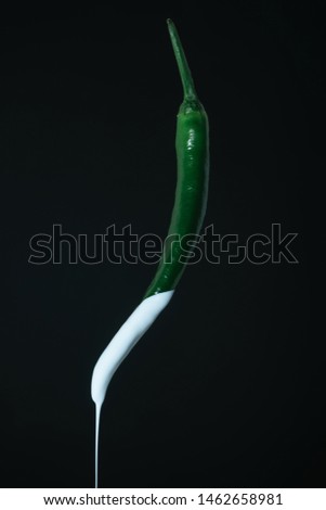 Dripping white paint of fresh green pepper on a black background. Creative poster.