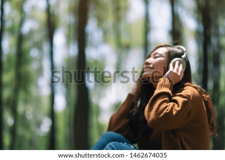 Blurred image of a beautiful asian woman enjoy listening to music with headphone with feeling happy and relaxed in the park