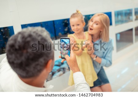 Daughter and wife. Grey-haired man taking photo of daughter and wife holding hamster in the pet shop