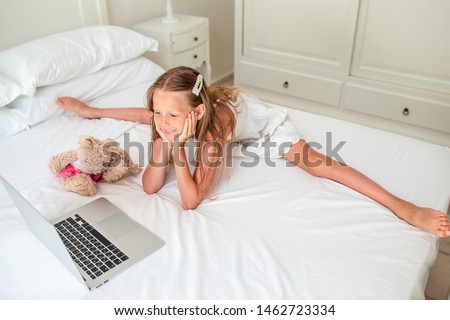 Little girl watching cartoons on computer on the bed