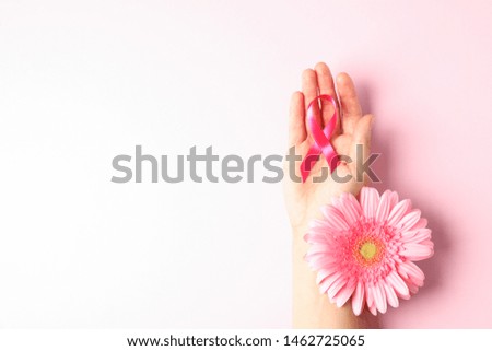 Female hand with pink awareness ribbon and gerbera color background