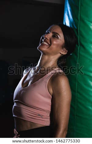 Young female boxer pose near bag on a sports training in a gym.