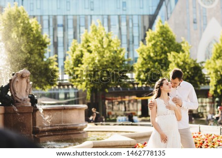 Loving husband gently hugging his pregnant wife. behind them is a fountain. Germany, Leipzig