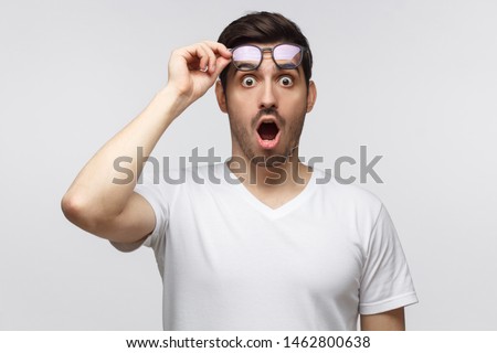 Young man in white t-shirt shouting, crabbed with shock content, holding eyeglasses with one hand Royalty-Free Stock Photo #1462800638