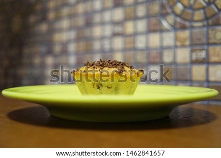 sweet breakfast. Cupcake with chocolate filings on top. Cake on a green saucer close-up. A plate stands on a wooden brown table. Mosaic wall in the background