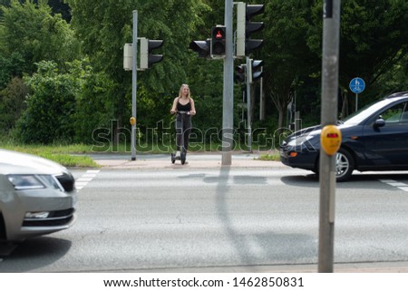 Young woman e-scooter on bike path at intersection with traffic light