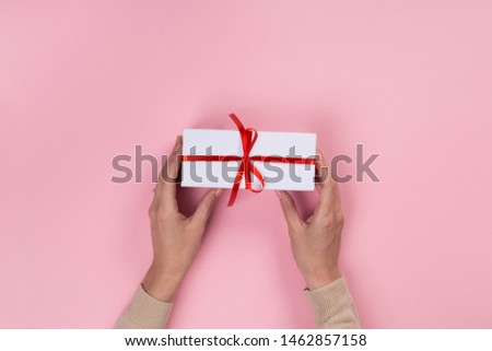 Womans hands holding gift or present box on pink pastel table top view. Flat lay  for birthday or New Year.