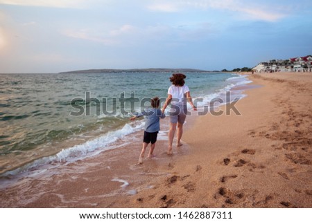 happy family, mother and son run along the sandy seashore in the summer at sunset, view from the back