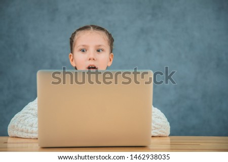 Cute little girl is looking at the screen of the computer and opens the mouth because of astonishment.