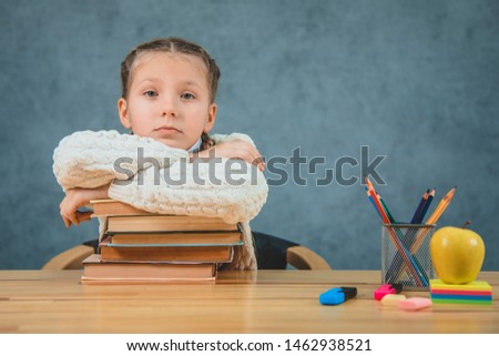 Cute blonde schoolgirl is lying down the books, tutorials, standing on the desk near green apple and colorful pencils.