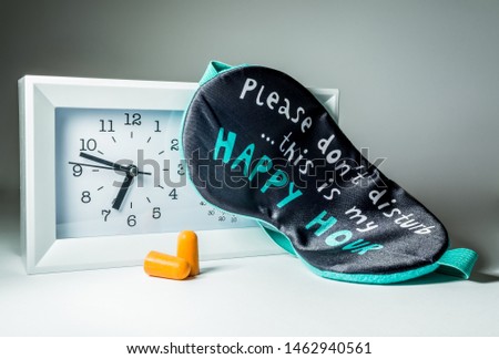 Modern clock with white alarm clock, funny sleep mask and earplugs close-up in the light of a night lamp.