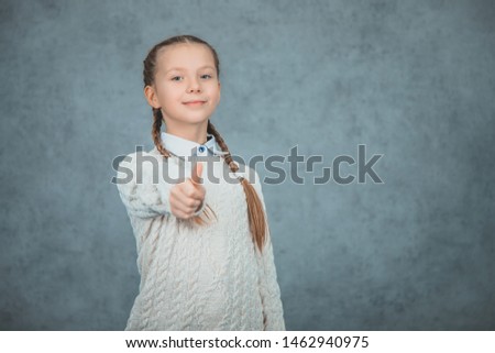 A happy and proud schoolgirl is gesturing thumb up is isolated on grey background.